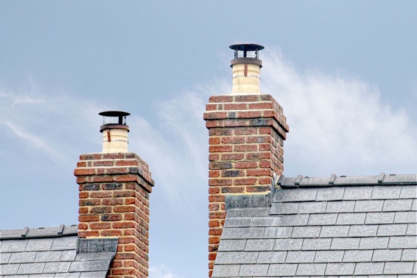 Traditional brick chimneys on a slate roof — height and access are what move chimney repair cost