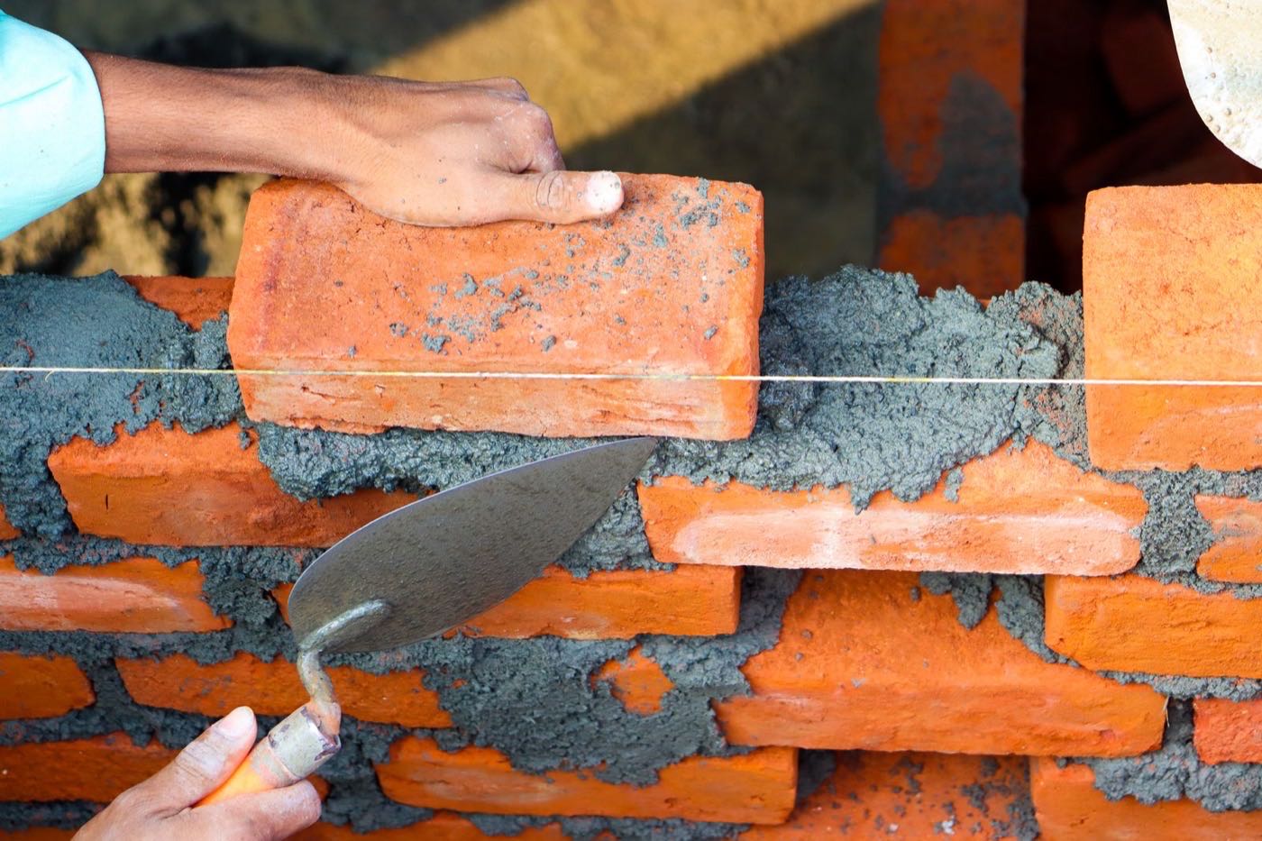 Mason's hands setting brick in fresh mortar — the heart of a repointing job